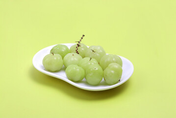 Gooseberry on a white plate on a yellow background