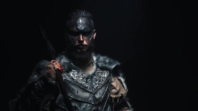 The brutal Viking cast his axe on his shoulder and shouts into the camera. A Scandinavian warrior in war paint puts an axe on his shoulder and shouts frighteningly at the camera