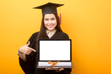 Beautiful woman in graduation gown is holding laptop mockup