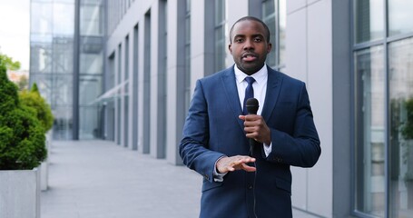 Portrait shot of young African American handsome male journalist talking with microphone for news...