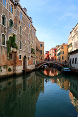 Fototapeta na wymiar Beautiful view of a canal between colorful stone buildings of Venice , Italy. There is a nice reflection of the street on the river.