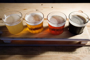 Beer samplers in small glasses individually placed in holes into a unique wooden tray and background. Amazing abstract colored lights in motion. Magical light in a glass of craft beer.