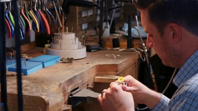 Jeweler working desk and man polishing a ring. Side shot as man sitting in front of the desk full of jeweler tool and polishes the ring.