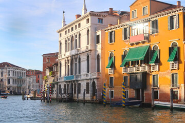 
Venice canal view at sunset. Sun reflects on the window of an orange building with green windows