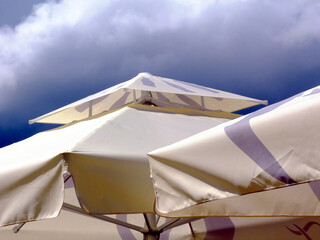  cream color canvas parasol and patio awning detail. blue and white sky on a sunny summer day. sun...