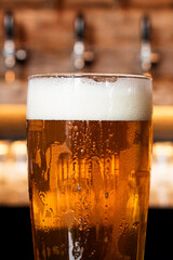 A cold glass of craft beer over a pub table with bokeh background. Happy hour time.