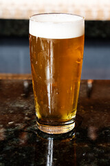 A cold glass of craft beer over a pub table with bokeh background. Happy hour time.