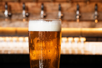 A cold glass of craft beer over a pub table with bokeh background. Happy hour time.