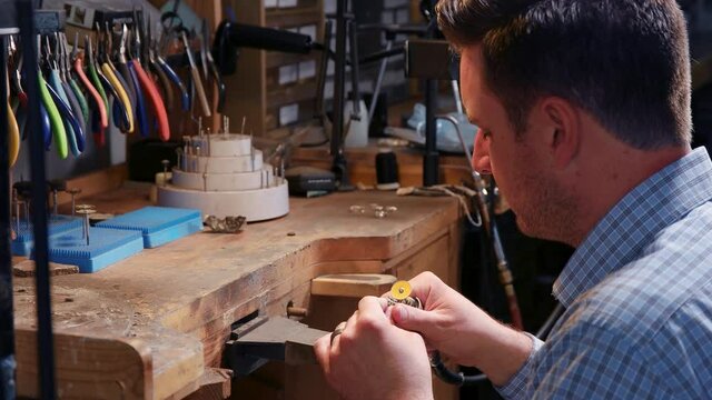 Jeweler holds the ring and polishes it with the rotary tool. Real time video as middle aged man is cleaning the ring with the stone.