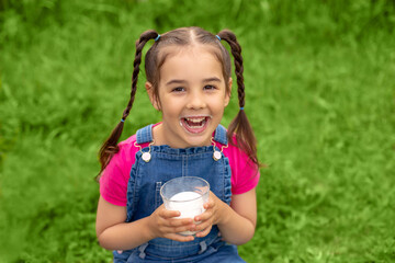 Portrait of a laughing girl with a glass of milk on a green lawn