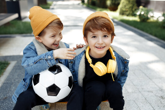 Two cute twin boys with happy faces sitting on the skateboard or pennyboard in the street.