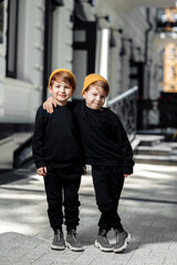 Two happy embraced twin boys posing with happy faces in the street.