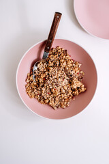 Granola muesli with pieces of chocolate in a pink plate on a white table. Healthly food, breakfast concept.