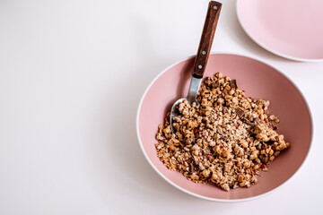 Granola muesli with pieces of chocolate in a pink plate on a white table. Healthly food, breakfast concept.