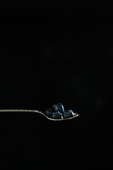 teaspoon with blueberries on black background