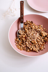 Granola muesli with pieces of chocolate in a pink plate on a white table. Healthly food, breakfast concept.