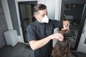Peluquero esteticista profesional cortando el pelo a clienta con las mascarilla de protección colocada por el virus COVID19