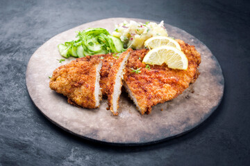 Traditionelles frittiertes Wiener Schnitzel aufgeschnitten mit Kartoffel und Gurken Salat angeboten...