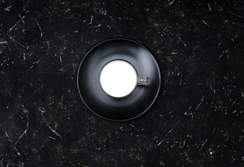 Glass of milk on a black matte plate on a textured black background. Top view, copy space. Milk for weight loss concept.