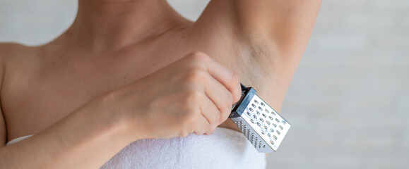Unrecognizable woman in a white terry towel holds a mini grater depicting shaving irritations. Female barbed armpit after depilation. Do hair removal of unwanted vegetation on the body.