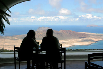 Silhuettes a couple of older people looking at a dream island throuth a cafe window