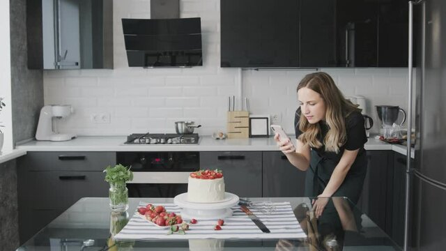 Confectionery blog. Woman in black shirt photographing cake decorated with strawberry.