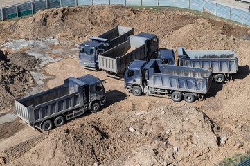 Aerial top view of several dump trucks unloading sand at a construction site. Industrial panorama.