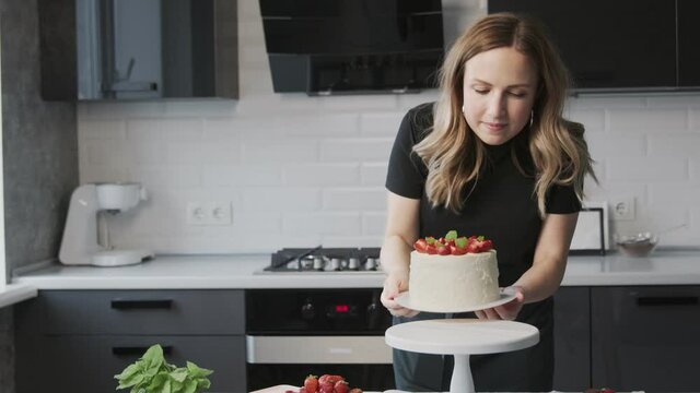 Confectionery blog. Woman in black shirt photographing cake decorated with strawberry.