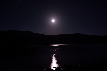 beautiful full moon over mountain in autumn night with reflection on fjord surface