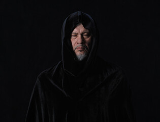 Naklejka na ściany i meble portrait of a medieval monk with a hood on a black background