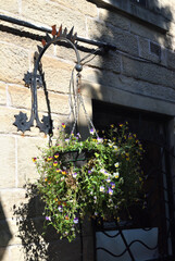 Fototapeta na wymiar Basket of Flowers Hanging from Ornate Bracket on Sunny Stone Wall