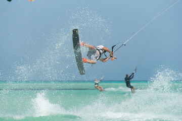 Naklejka premium kiter does a difficult trick on a background of transparent water and blue sky
