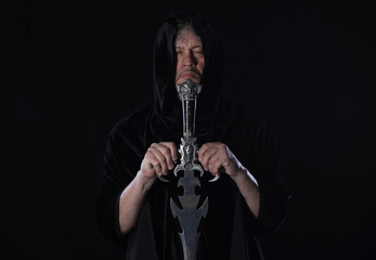 portrait of a medieval warrior in a hood with a sword on a black background