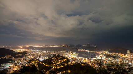 Wide night view over Rio de Janeiro looking at the bay and Sugarloaf Mountain with the city glowing.