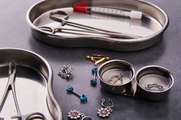 Piercing tools lie in a stainless steel disinfection container on a black background