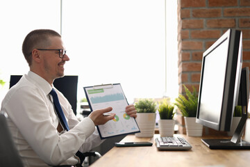 Portrait of cheerful stylish businessman showing monthly report on camera. Man talking on video...