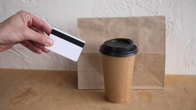 cropped view of man showing credit card near paper bag and disposable cup