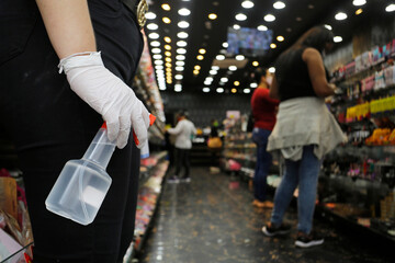 A woman holds a bootle of hand sanitizer due to Coronavirus outbreak, COVID-19, as she wait for customers at the entrance of a store in Sao Paulo, Brazil.
