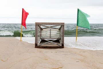 Lifeguard stand lying on sand between green and red flags with ocean waves in background