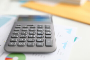 Close-up of black calculator laying on business papers. Equipment to calculate numbers. Tool with buttons on working desktop. Financial report and statistics concept