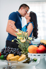 Happy married couple kissing in the kitchen surrounded with fruits.