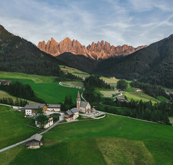 Beautiful village in the Alps. Santa Magdalena on Dolomites Background. Sunset in the mountains in Italy. Red peaks of mountains. Top view by drone.