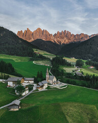 Beautiful village in the Alps. Santa Magdalena on Dolomites Background. Sunset in the mountains in Italy. Red peaks of mountains. Top view by drone.