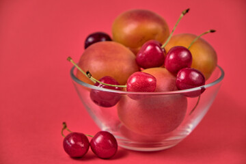 Fresh juicy apricots and red sweet cherries in a transparent glass plate. Macro.