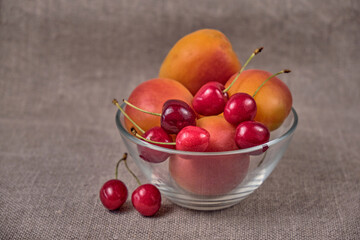 Fresh juicy apricots and red sweet cherries in a transparent glass plate. Macro.