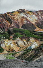Colored rainbow mountains in Iceland. A traveler with a backpack in bright clothes goes to the mountains. Epic view of the Landmannalaugar Valley. Adventure and travel content.