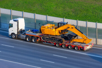 Heavy new yellow excavator on transportation truck with long trailer platform on the highway in the...