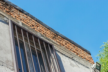 Obraz premium Part of an old industrial building with windows on which there are metal bars. Blue sky and bright sunlight on a hot summer day. Walks around the city in the summer.
