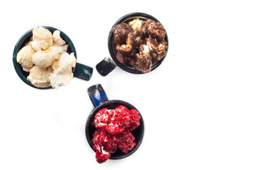 Rustic colored cups of Chocolate, Strawberry and Cream Gourmet Popcorn over white background.