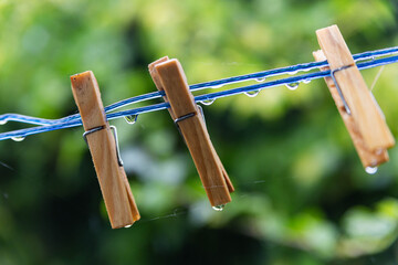Close up of wooden pegs on a blue rain drenched washing line, with water droplets and green bokeh background